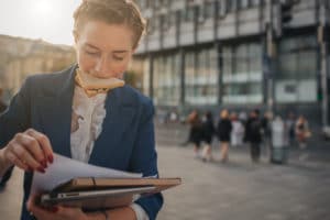 A woman with a donut in her mouth reading papers.