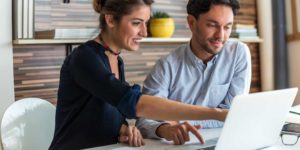 A woman and man sitting at a table with a laptop.